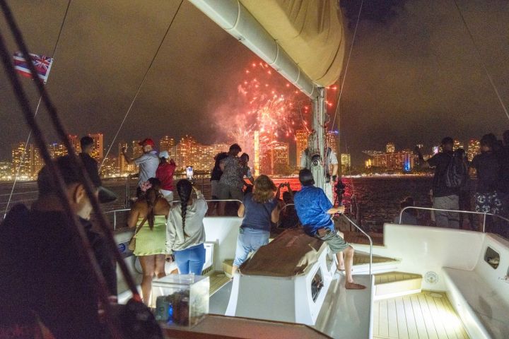 People on a boat watching fireworks over a city skyline at night.