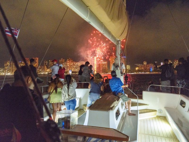 People on a boat watching fireworks over a city skyline at night.