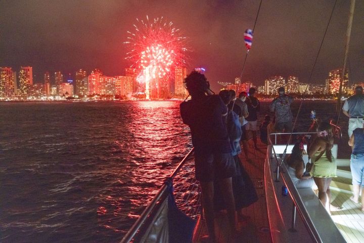 People on a boat watching fireworks over a city skyline at night.