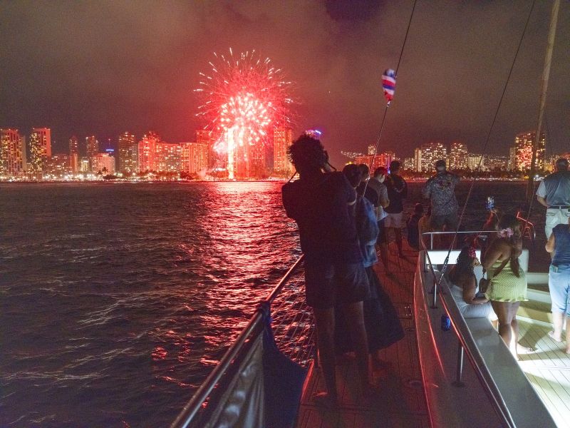 People on a boat watching fireworks over a city skyline at night.