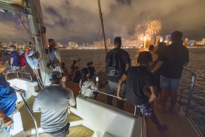 People on a boat watching fireworks over a city skyline at night.