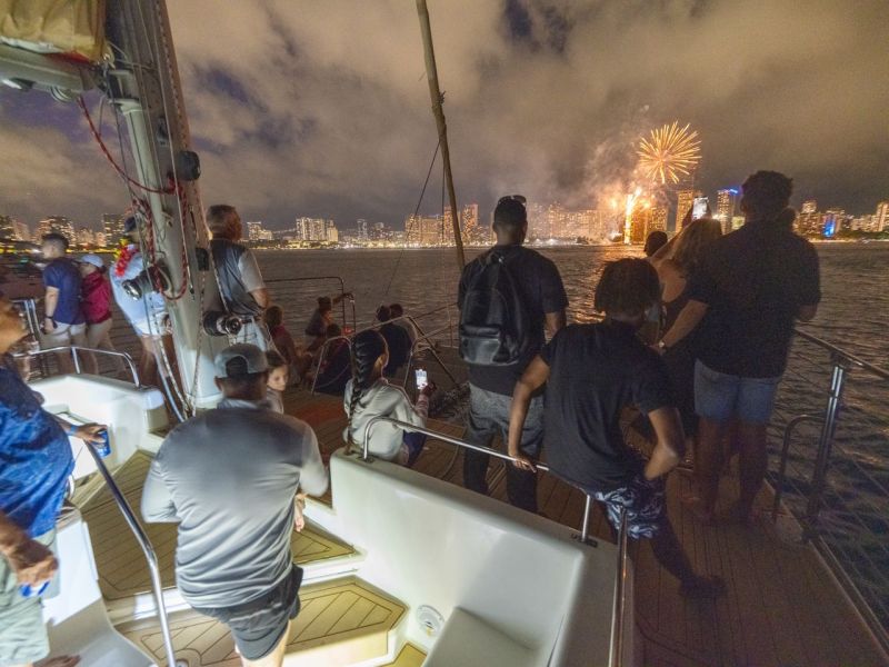 People on a boat watching fireworks over a city skyline at night.