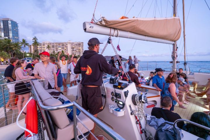 People enjoying a party on a sailboat near the beach at sunset.