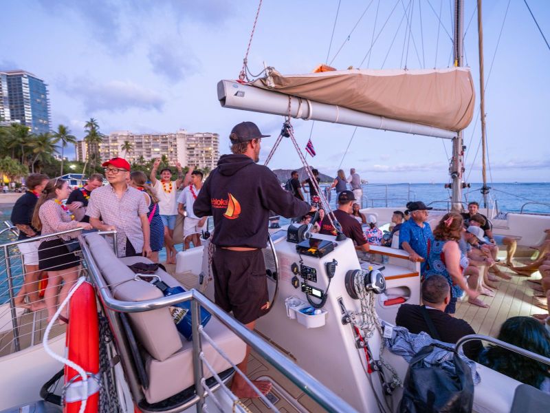 People enjoying a party on a sailboat near the beach at sunset.
